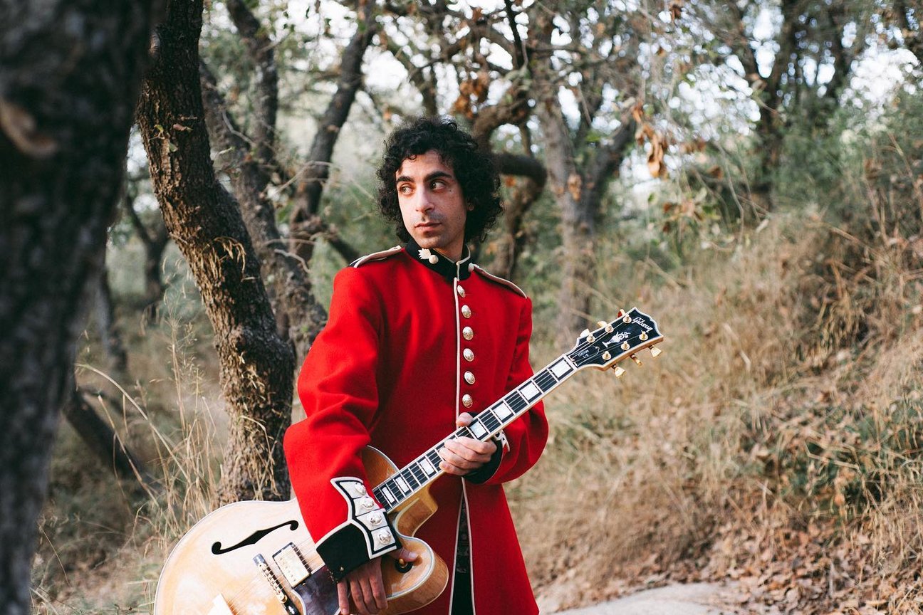 Aviram photographed with a guitar in a red jacket